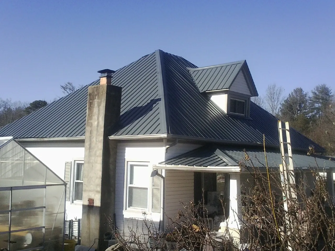 Dark blue standing seam metal roof on a white farmhouse with dormer — Slate & Tile Roof Repair by Roofing Brothers in Pacific Palisades