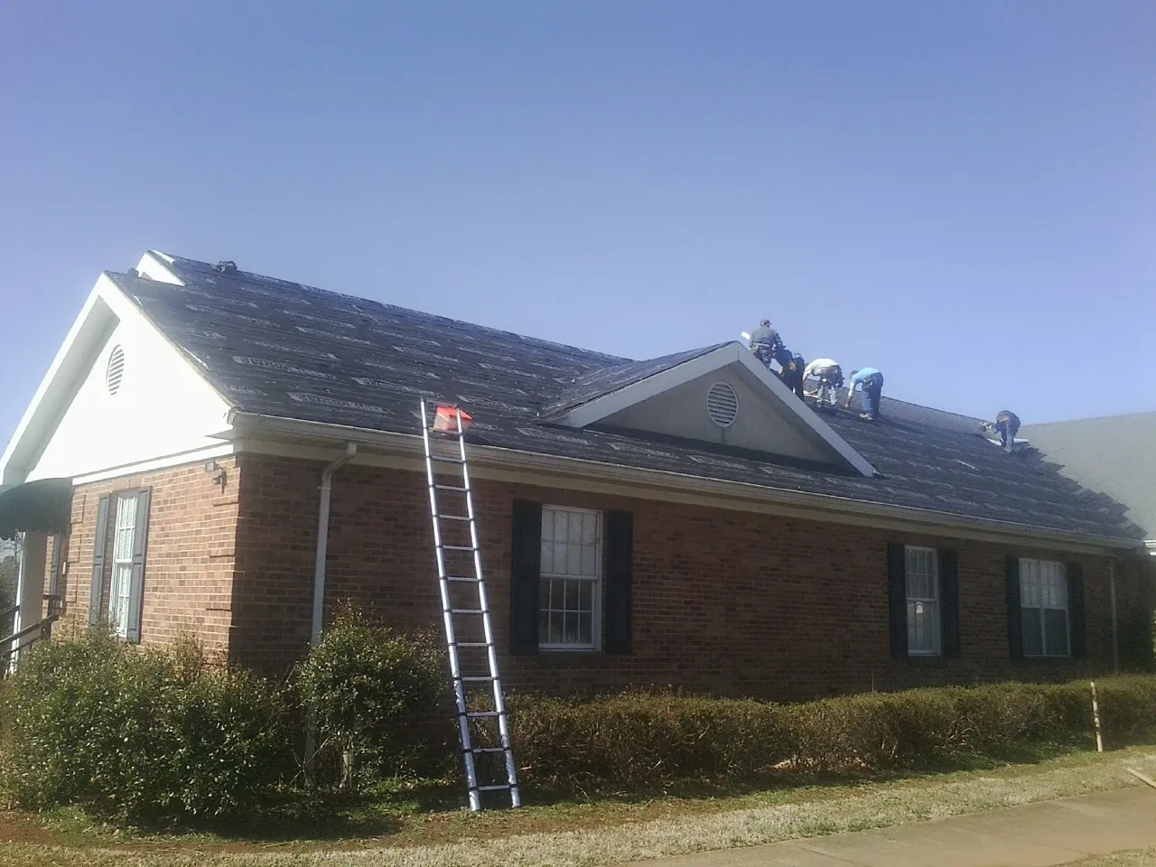 Crew tearing shingles off a brick ranch roof with a ladder set — Emergency Roof Repair work by our crew in Pacific Palisades