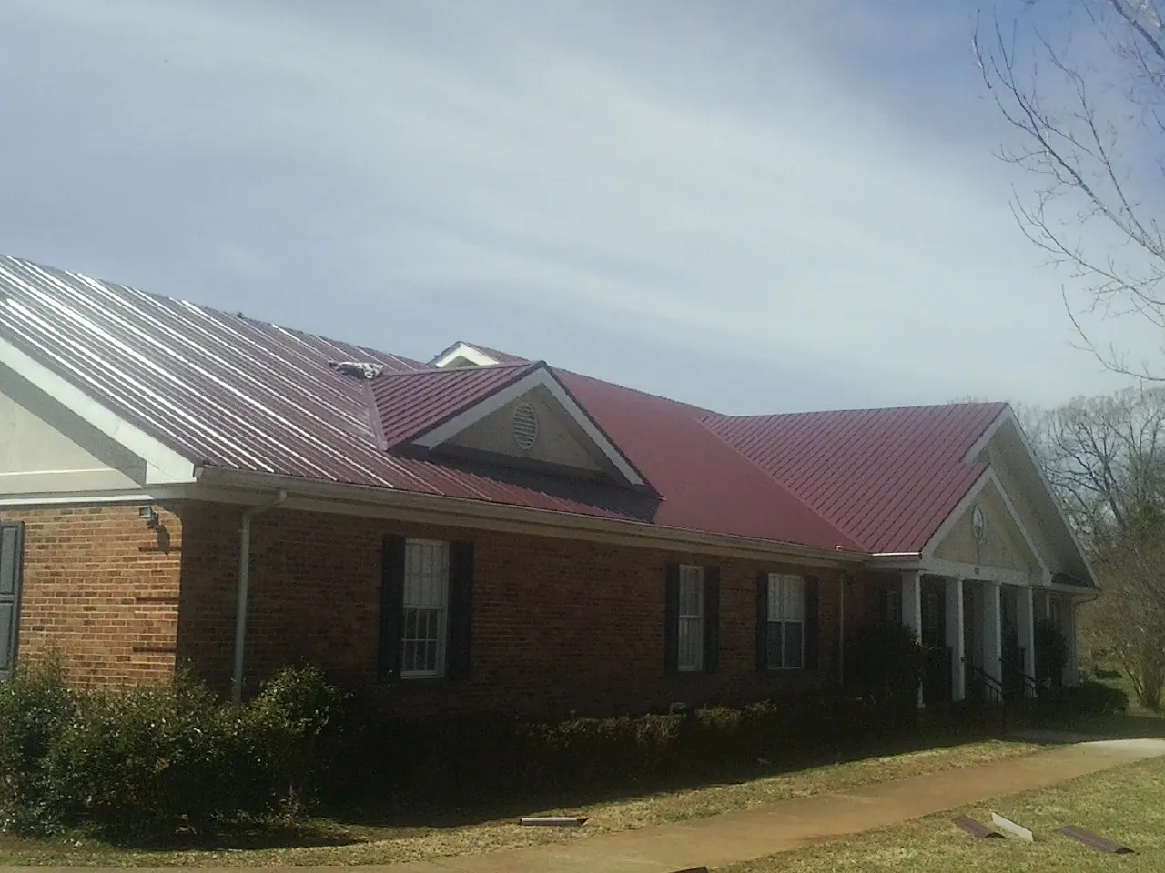 Red metal roof with gabled entries on a long brick building, from a Hail Damage Roof Repair job in Pacific Palisades